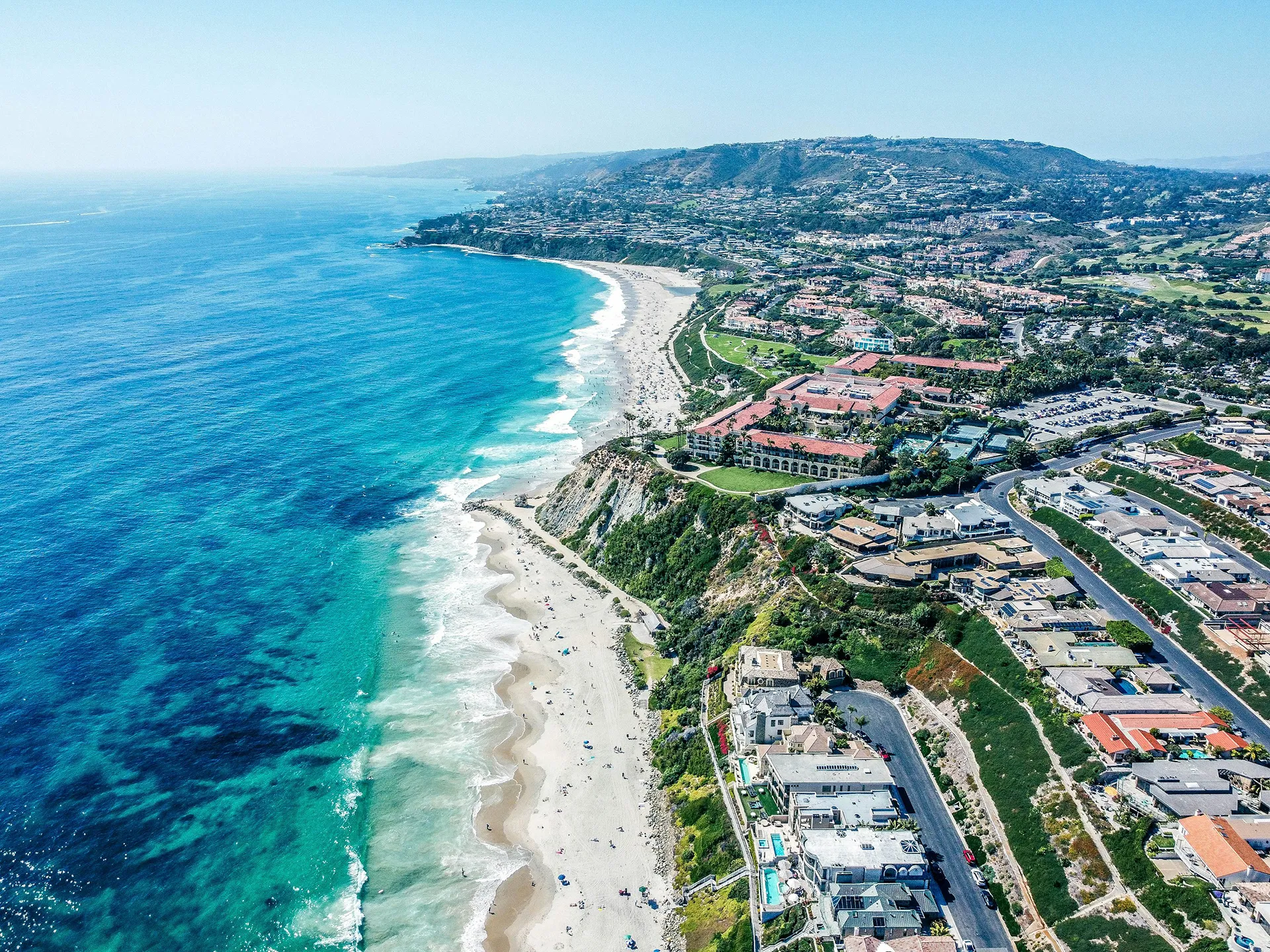 Aerial view of coastline with beach, homes, and blue ocean water, real estate.