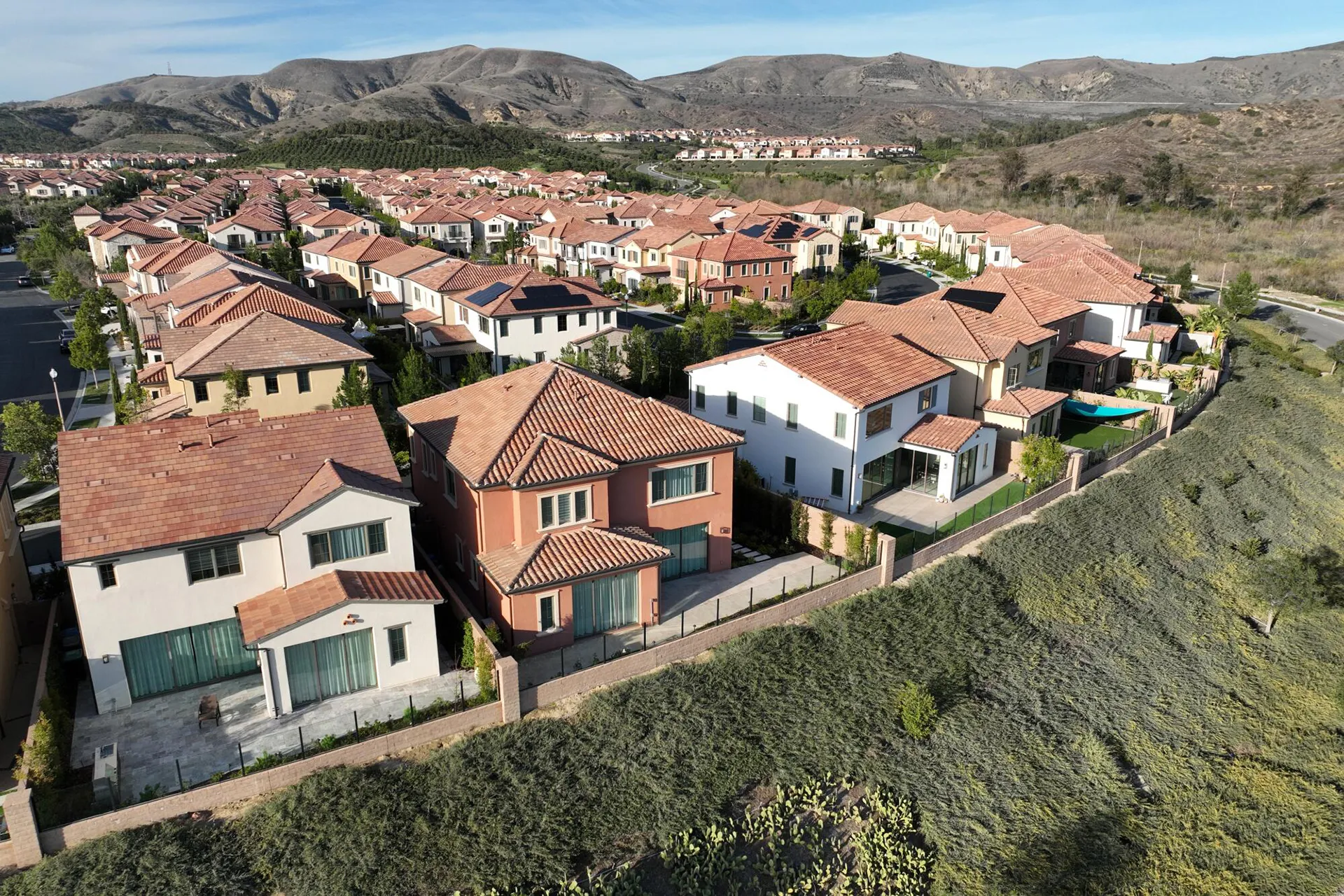 Aerial view of neighborhood with houses, yards, mountains, and open land, real estate.